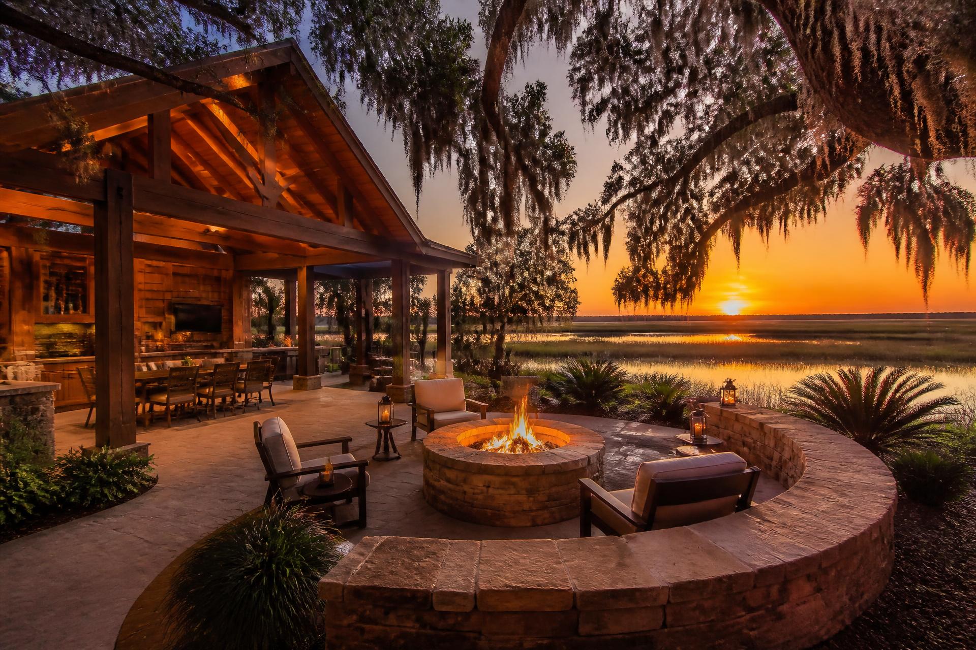 Cedar pavilion, fire pit and stone seat wall overlooking a marsh at sunset beneath moss-draped live oaks